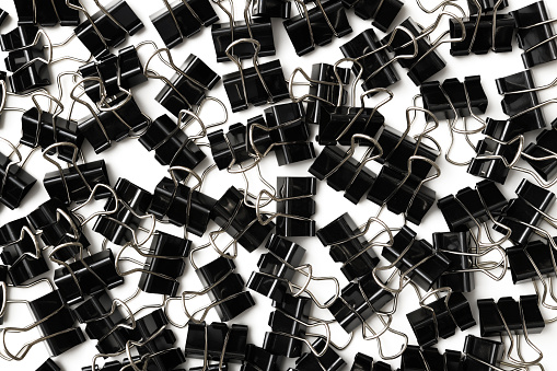 Overhead shot of many black paper clip on white background.
