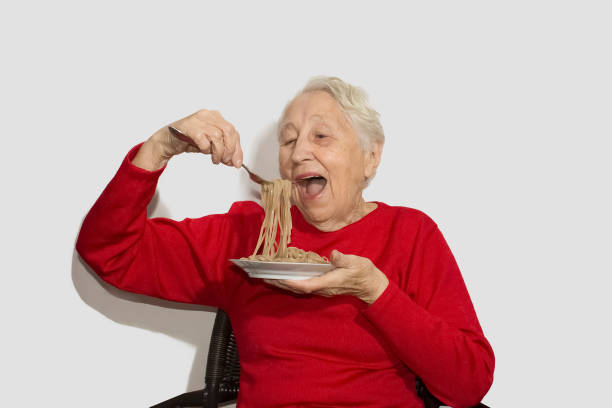happy senior woman eating italian spaghetti pasta isolated on white studio - eating senior adult color image spaghetti imagens e fotografias de stock