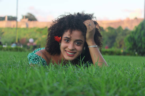 A Cuban woman is lying on the grass and enjoys nature. The young woman has a green dress