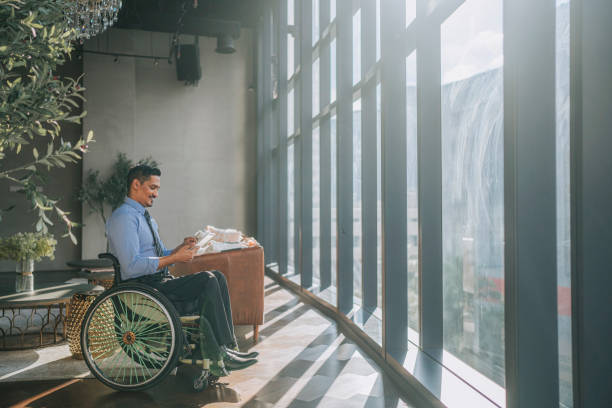 istock disable Asian Indian male white collar worker in wheelchair reading digital tablet smiling at lounge area smiling 1356508176