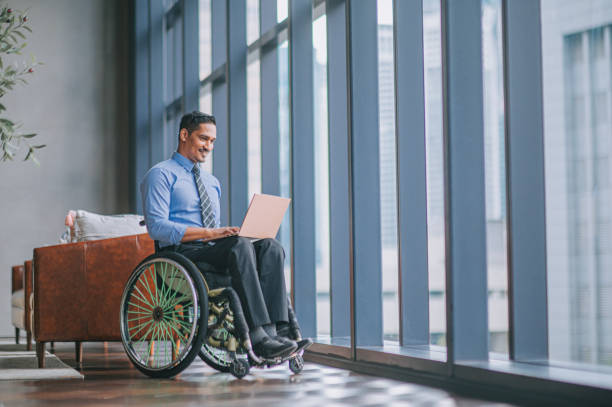 istock disable Asian Indian male white collar worker in wheelchair using laptop smiling at lounge area 1356508200