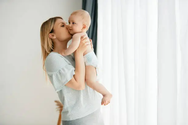 Photo of Loving mother kissing her baby while spending time together at home.