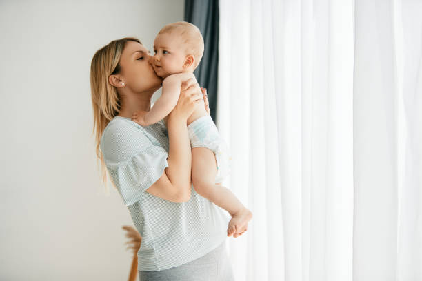 любящая мама целует своего малыша, проводя время вместе дома. - младенец стоковые фото и изображения