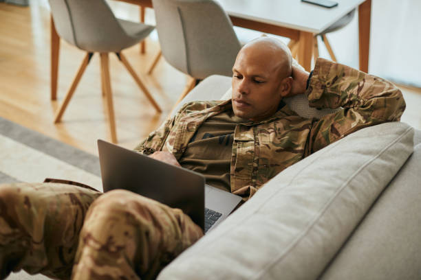 African American soldier using laptop while relaxing on the sofa at home.