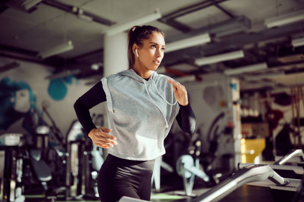 entschlossene athletische frau, die auf dem laufband läuft, während sie in einem fitnessstudio übt. - sportlerin stock-fotos und bilder