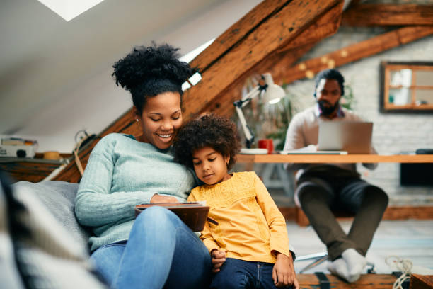 istock Happy African American mother and daughter using digital tablet while relaxing at home. 1356510535