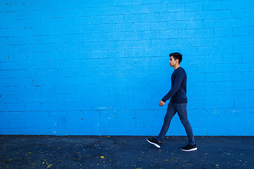 Portrait of the young man walking against blue background