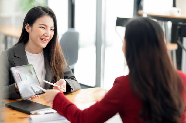 istock Two young attractive asian woman using tablet and discussing about business plan together while sitting at office. 1356524185