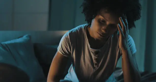 Depressed african american woman sitting on bed, she is suffering from insomnia