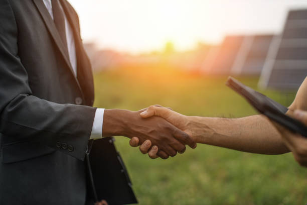Technician and businessman shaking hands on solar plant