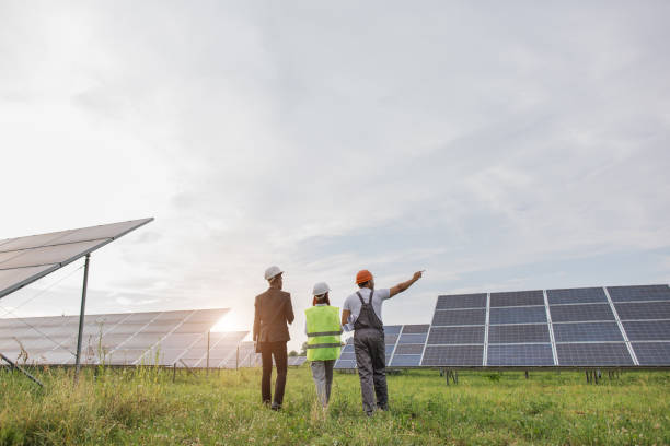 rückansicht von drei arbeitern, die auf der solarstation spazieren gehen - panel dicussion stock-fotos und bilder