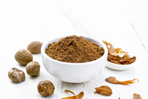 Nutmeg ground in bowl and mace in spoon on light board Ground nutmeg in a bowl and dried nutmeg arillus in a spoon, whole nuts on wooden board background mace spice stock pictures, royalty-free photos & images