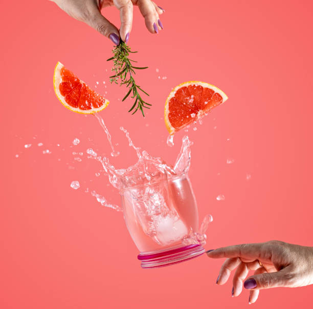Woman hand support fly glass of grapefruit drink with splash, juice grapefruit slices falling in glass. Cocktail of grapefruit, thyme and rosemary flavor Woman hand support fly glass of grapefruit drink with splash, juice grapefruit slices falling in glass. Cocktail of grapefruit, thyme and rosemary flavor. Summer art food concept on pink background carbonated juice stock pictures, royalty-free photos & images