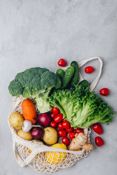 istock Mesh bag with vegetables. Organic broccoli, tomato, cucumbers, carrot, onions, lemon, garlic, ginger, lettuce and potato in cotton shopper bag 1356530761