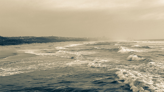 Morning mood along beach coastline with ocean sea waves next to river mouth windy choppy white water with cloudy sky in sepia photo horizon landscape.