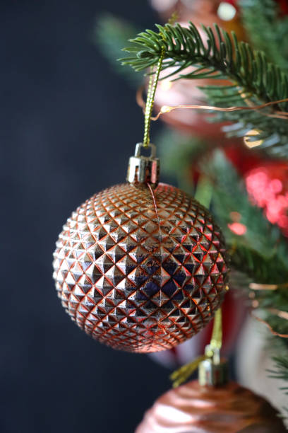 istock Close-up image of individual, copper, textured bauble hanging on artificial Christmas tree branch, spruce needles, blurred white fairy lights background, copy space 1356531886