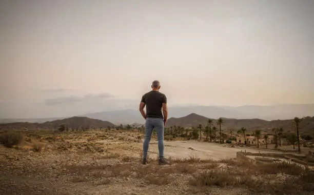 Adult man in Tabernas desert, Almeria, Spain, with an abandoned village in summer