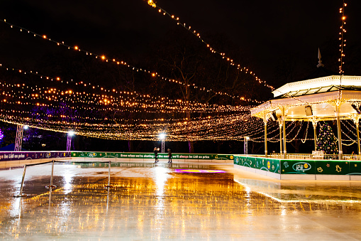 London, England - November 2021: they ice skate at the Winter Wonderland in Hyde Park at night. The ice rink is illuminated with beautiful Christmas lights throughout. The Winter Wonderland is one of the most exciting outdoor Christmas events of the season in London.