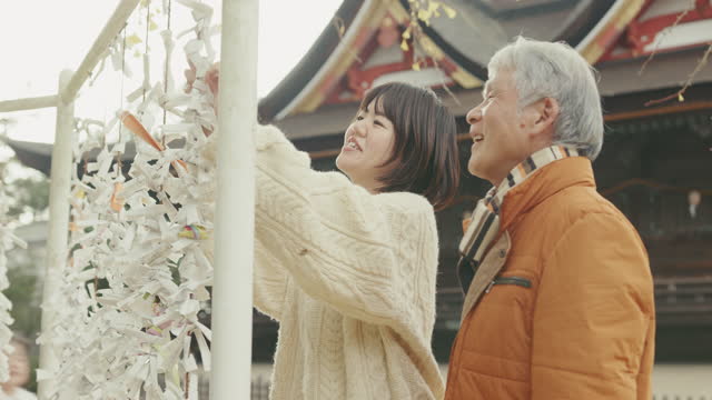 MCU- Senior father and adult daughter tying fortune paper at a Japanese temple