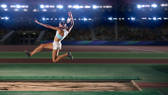Female fit caucasian runner in sportswear running fast and jumping through hurdle at stadium track wide shot
