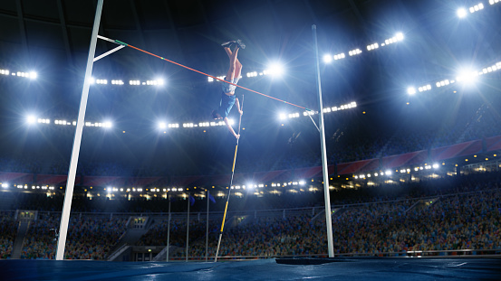 Young female athlete in pole vault action against the cloudy blue sky and late afternoon sunlight