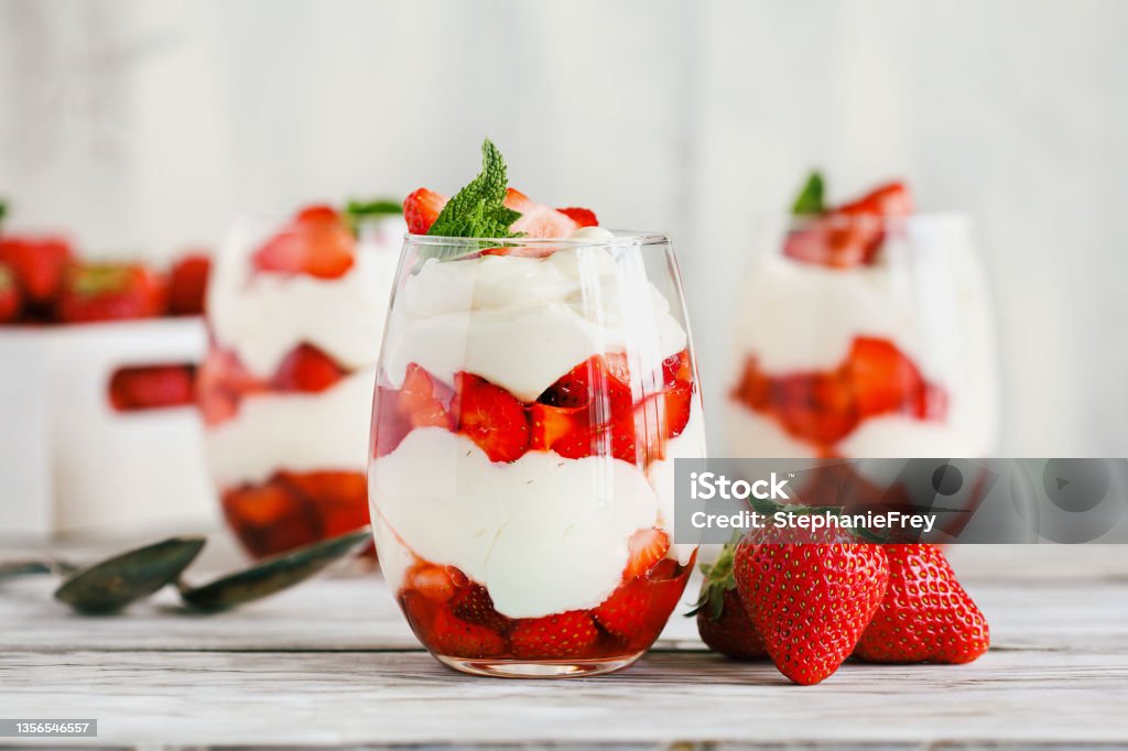 Healthy breakfast of strawberry parfait made with fresh fruit, and yogurt over a rustic white table Healthy breakfast of strawberry parfaits made with fresh fruit, and yogurt over a rustic white table. Selective focus on glass jar in front. Blurred background and foreground. Strawberry Stock Photo
