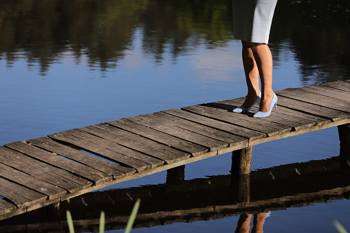 cropped photo of female legs walking on a wooden pier on the river.