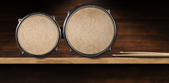 Close-up of bongo drums and a pair of drumsticks, above a wooden shelf with copy space. Percussion instrument. Photography.