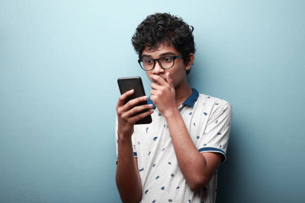 joven de origen indio mirando su teléfono móvil con una expresión de rostro sorprendido - photography teenagers only vertical teenager fotografías e imágenes de stock