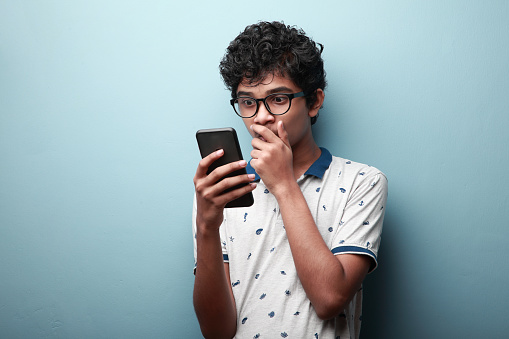 Young boy of Indian origin looking at his mobile phone with a surprised face expression