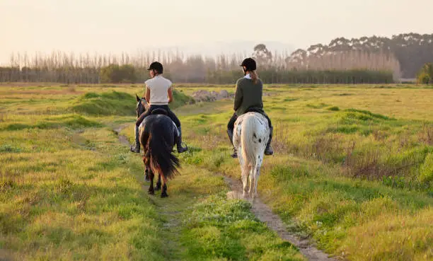 Photo of Shot of two unrecognizable woman riding their horses outside on a field