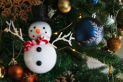 Stock photo showing a close-up view of artificial Christmas tree with spruce needles, gold, copper and blue themed decorations and white fairy lights.