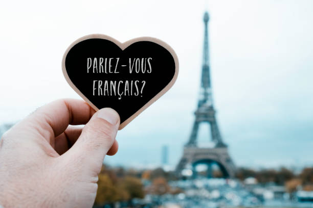 question do you speak French, in French, in Paris closeup of a young man holding a heart-shaped signboard with the question do you speak French written in French in it, in front of the Eiffel Tower in Paris, France french language photos stock pictures, royalty-free photos & images