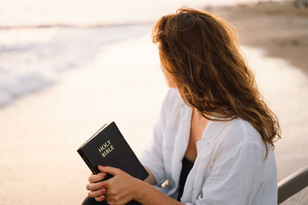 la donna cristiana tiene la bibbia nelle sue mani. leggere la sacra bibbia sul mare durante il bellissimo tramonto. concetto di fede, spiritualità e religione. - please god foto e immagini stock