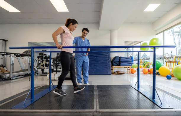 Woman in physical therapy walking on the parallel bars Latin American woman in physical therapy walking on the parallel bars with the assistance of his therapist physiotherapy stock pictures, royalty-free photos & images