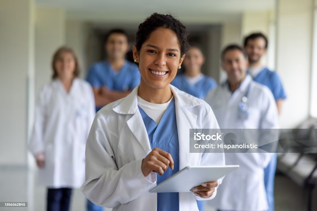 Happy doctor leading a team of healthcare workers at the hospital Happy female doctor leading a team of healthcare workers at the hospital and looking at the camera smiling Doctor Stock Photo
