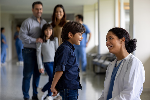 Happy Latin American pediatrician talking to a boy at the hospital and smiling - pediatric ward concepts