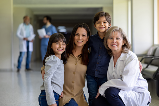 Happy Latin American family smiling at the hospital with a doctor while looking at the camera - healthcare and medicine concepts