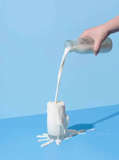 Photo of Pouring milk into the glass on a blue background. Spilled milk on the table.