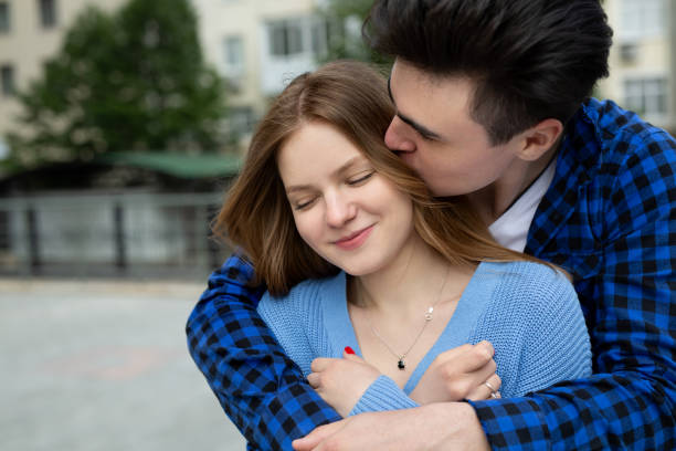 Cute young woman clung closely to her boyfriend, they are standing on the park stairs
