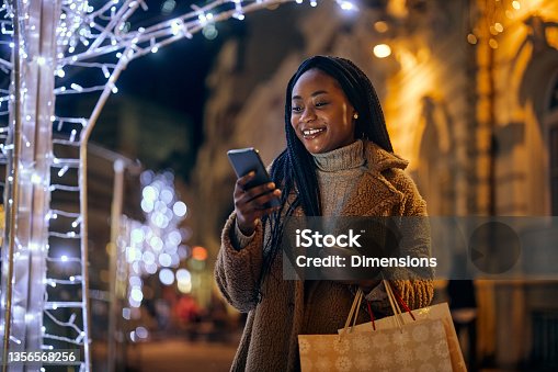 istock Afro woman holding shopping bags and looking at her phone 1356568256