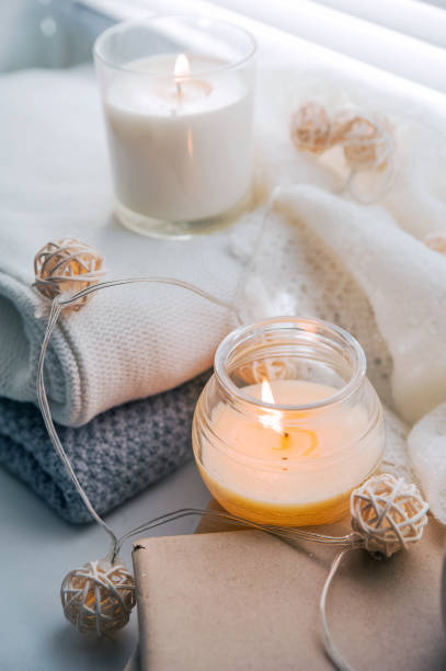 istock Burning candles and white sweaters on windowsill. Cozy autumn and winter concept, window with blinds... 1356569822