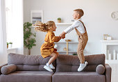 Overjoyed little children brother and sister jumping on sofa at home