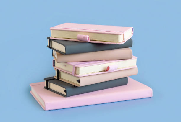 istock Stack of pink, beige and grey notebooks on light blue closeup 1356573686