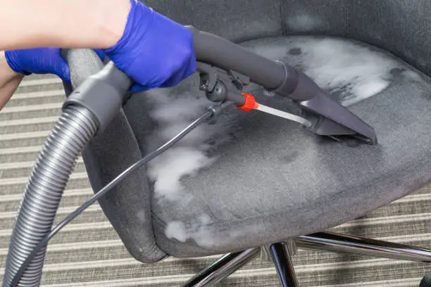 wet cleaning of the chair with a cleaning vacuum cleaner and thick foam, hands in protective gloves