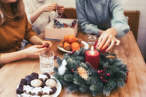 three young woman decorating together advent wreath on wooden table in the kitchen