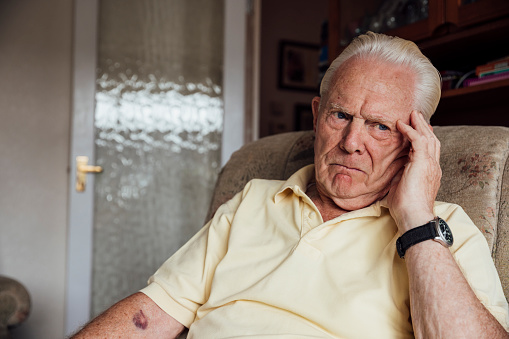 Senior man who has a chronic illness/Alzheimer's disease at his home in the North East of England. He is looking away from the camera with a negative expression, experiencing anxiety/pain.