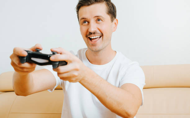 istock Happy young man playing video game with joystick, enjoying active leisure while sitting on sofa at home. Joyful guy player gamer with gamepad and hobby electronic sport 1356590280