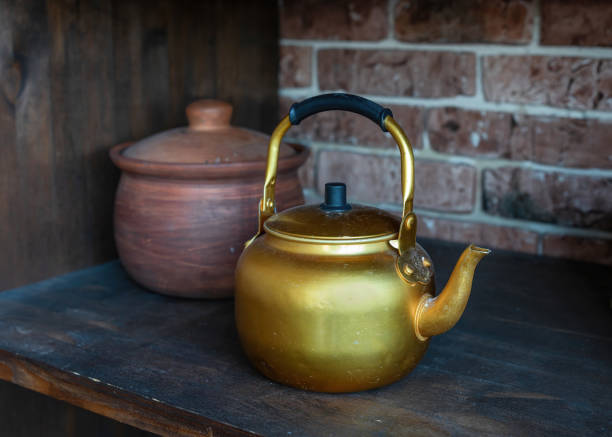 istock Ancient gold kettle on old wooden shelf. Classic teapots to use for drinking tea or coffee. Clay pot in the background 1356594385