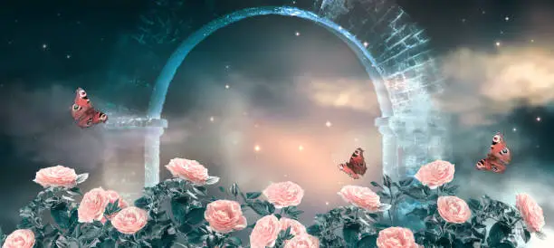 Photo of Fantasy fabulous panoramic background of night sky with stars, clouds and roses garden and peacock eye butterflies against magical mirage of old stone ruins of ancient gate